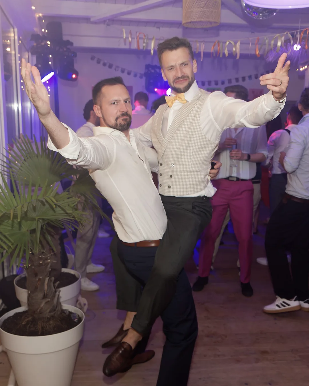 Dominik und Felix auf einer Feier, beide im weißen Hemd, mit ausgebreiteten Armen auf der Tanzfläche